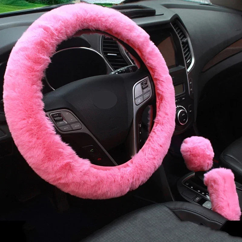A pink plush steering wheel cover installed on a car steering wheel, with coordinating covers for gear shift and handbrake.